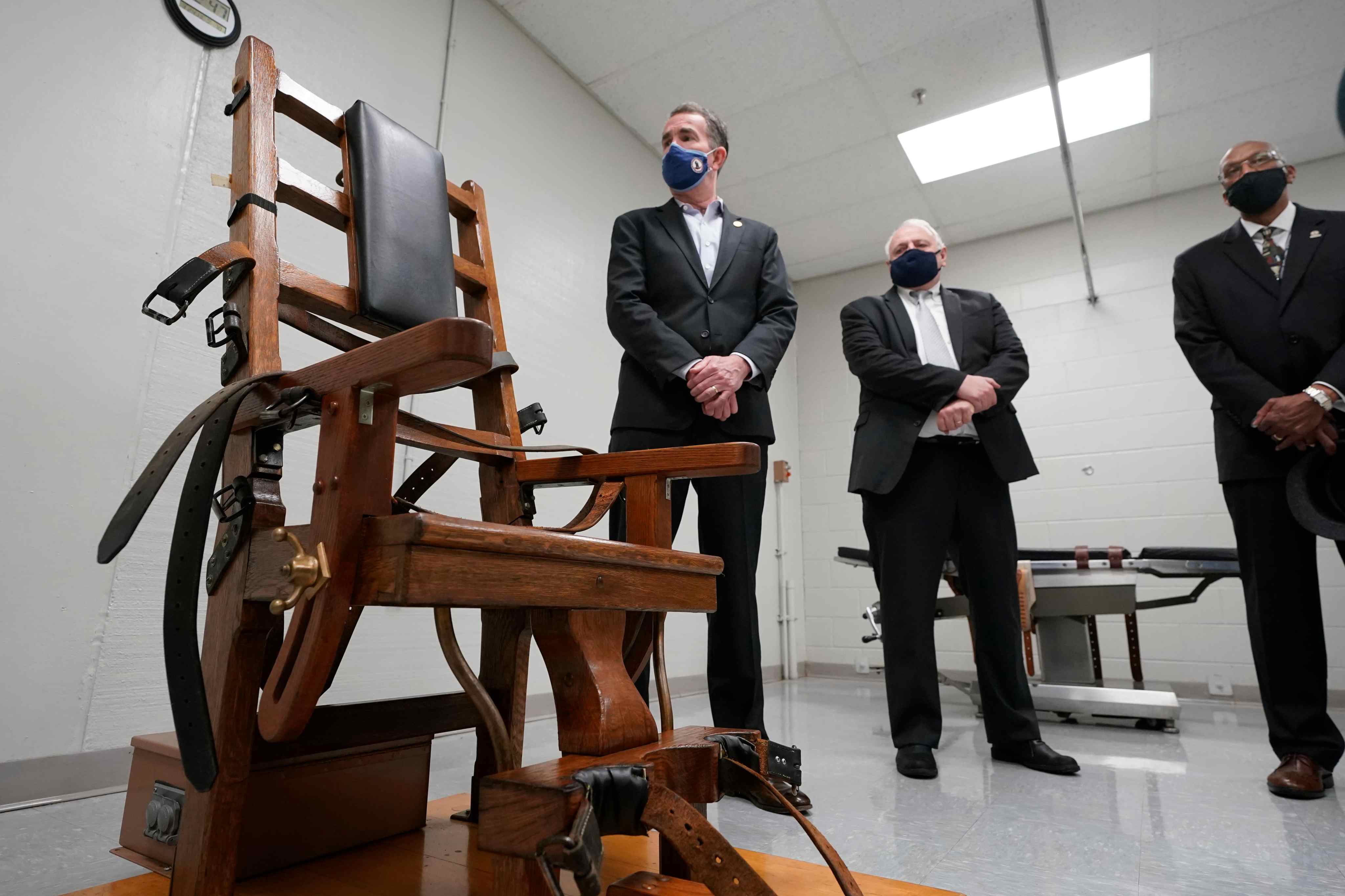 Virginia Gov. Ralph Northam, left, looks over the electric chair in the death chamber at Greensville Correctional Center with Operations Director, George Hinkle, center, and Director of the Department of Corrections, Harold Clarke, right, prior to signing a bill abolishing the penalty in Jarratt, Va., Wednesday, March 24, 2021. One hundred and two executions were performed at the since the early 1990's. (AP Photo/Steve Helber)