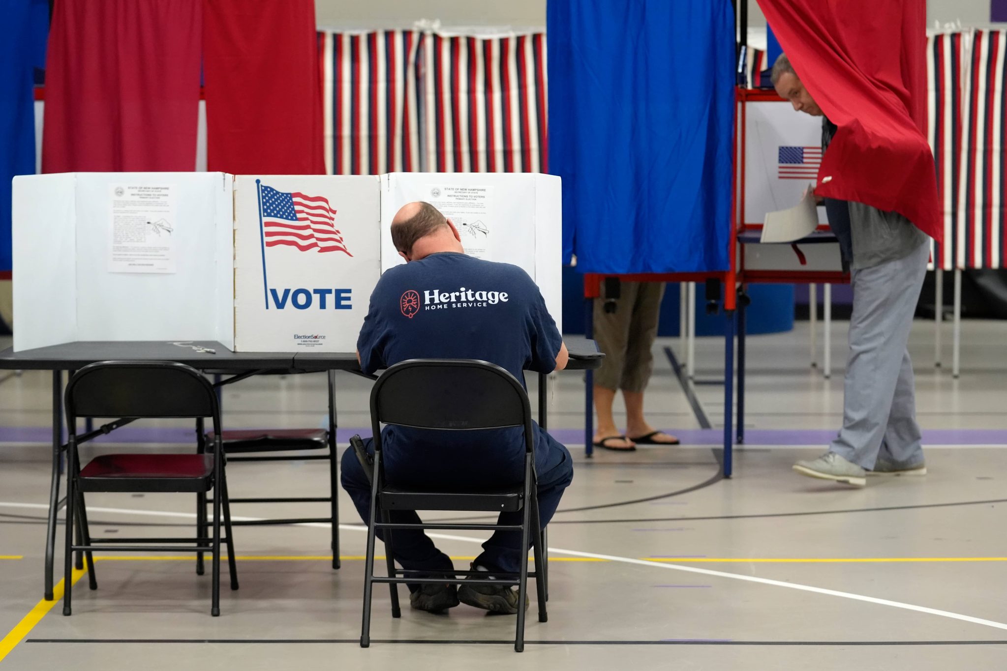 A voter, seen from behind, sits at a voting table to fill out a ballot.